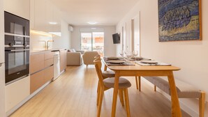A modern kitchen with built-in appliances, a dining area with a wooden table and chairs, and a large painting on the wall.