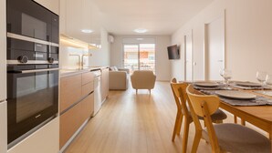 A modern kitchen with built-in appliances, a dining area with a wooden table and chairs, and a view of the outside.
