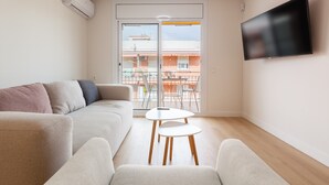 A modern living room with a sofa, a small table, a flat-screen TV, and a sliding glass door leading to an outdoor balcony.