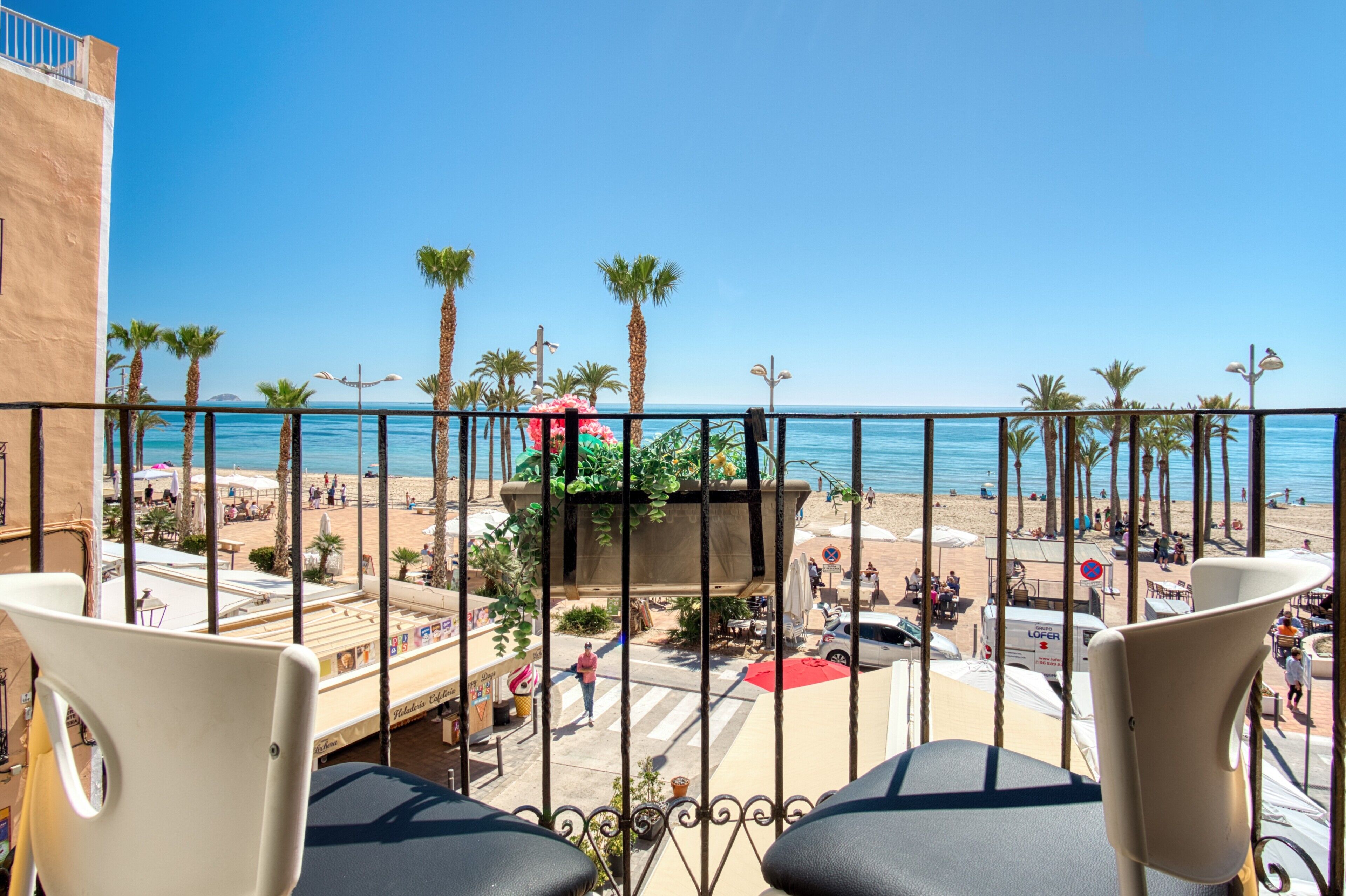 Un balcón con vista a una playa, palmeras y un vehículo LOFTER.