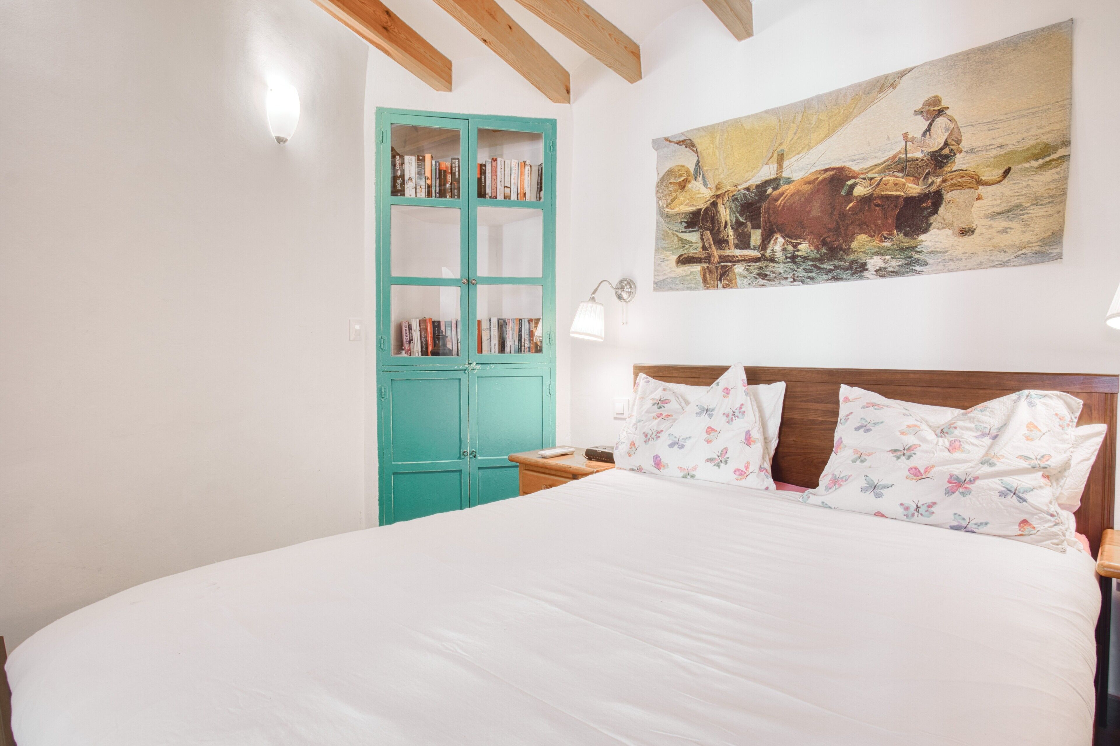 A bedroom with a large bed, a teal wardrobe, a painting of a bull, and a nightstand.