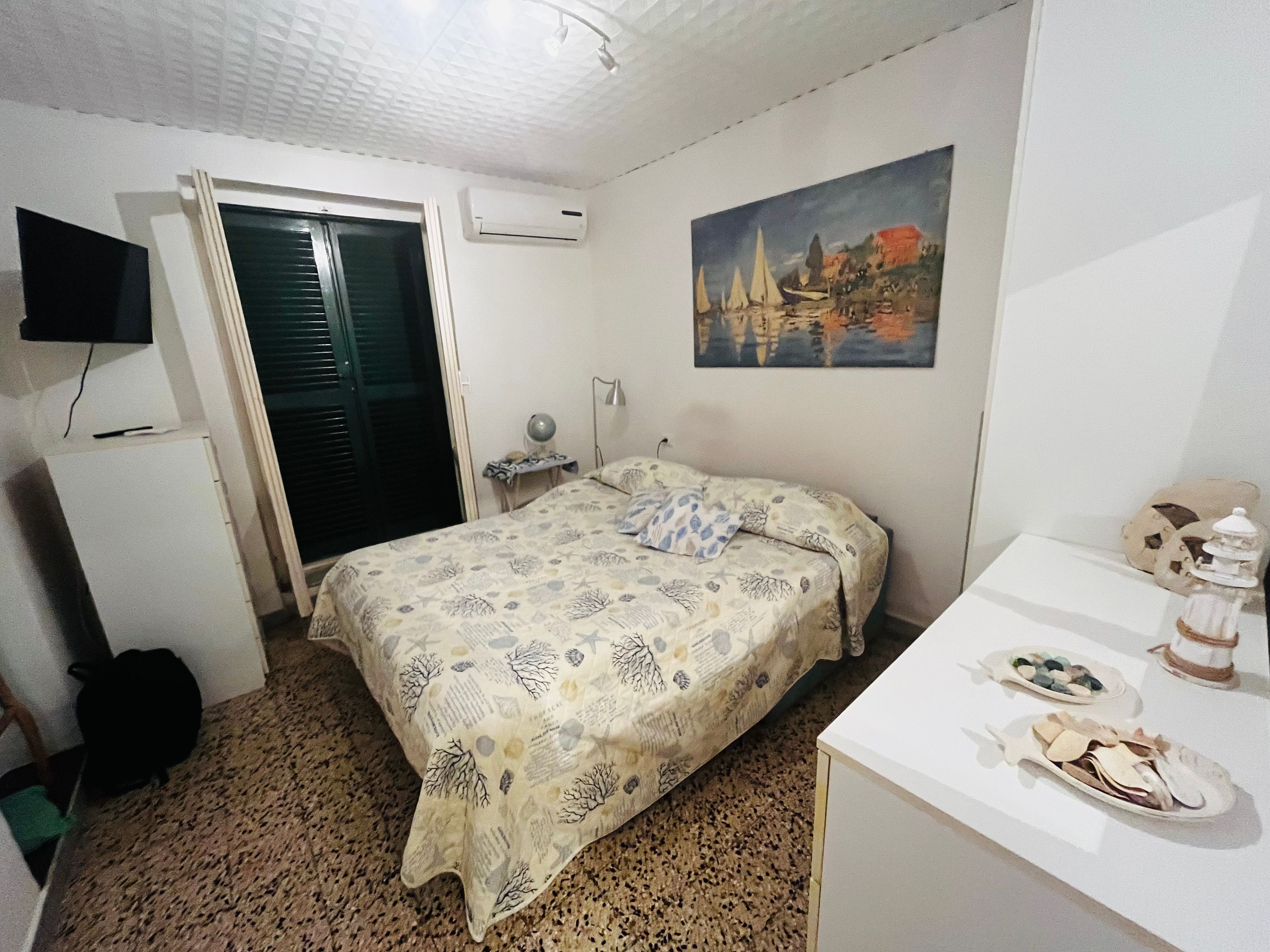 Ein Schlafzimmer mit Bett, Schreibtisch, Stuhl, Fernseher und einem Bild an der Wand.
