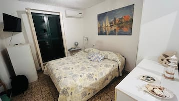 Ein Schlafzimmer mit Bett, Schreibtisch, Stuhl, Fernseher und einem Bild an der Wand.