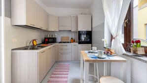 Eine kompakte Küche mit modernen Geräten, ein Essbereich mit Tisch und Stühlen sowie ein Fenster mit Vorhängen.