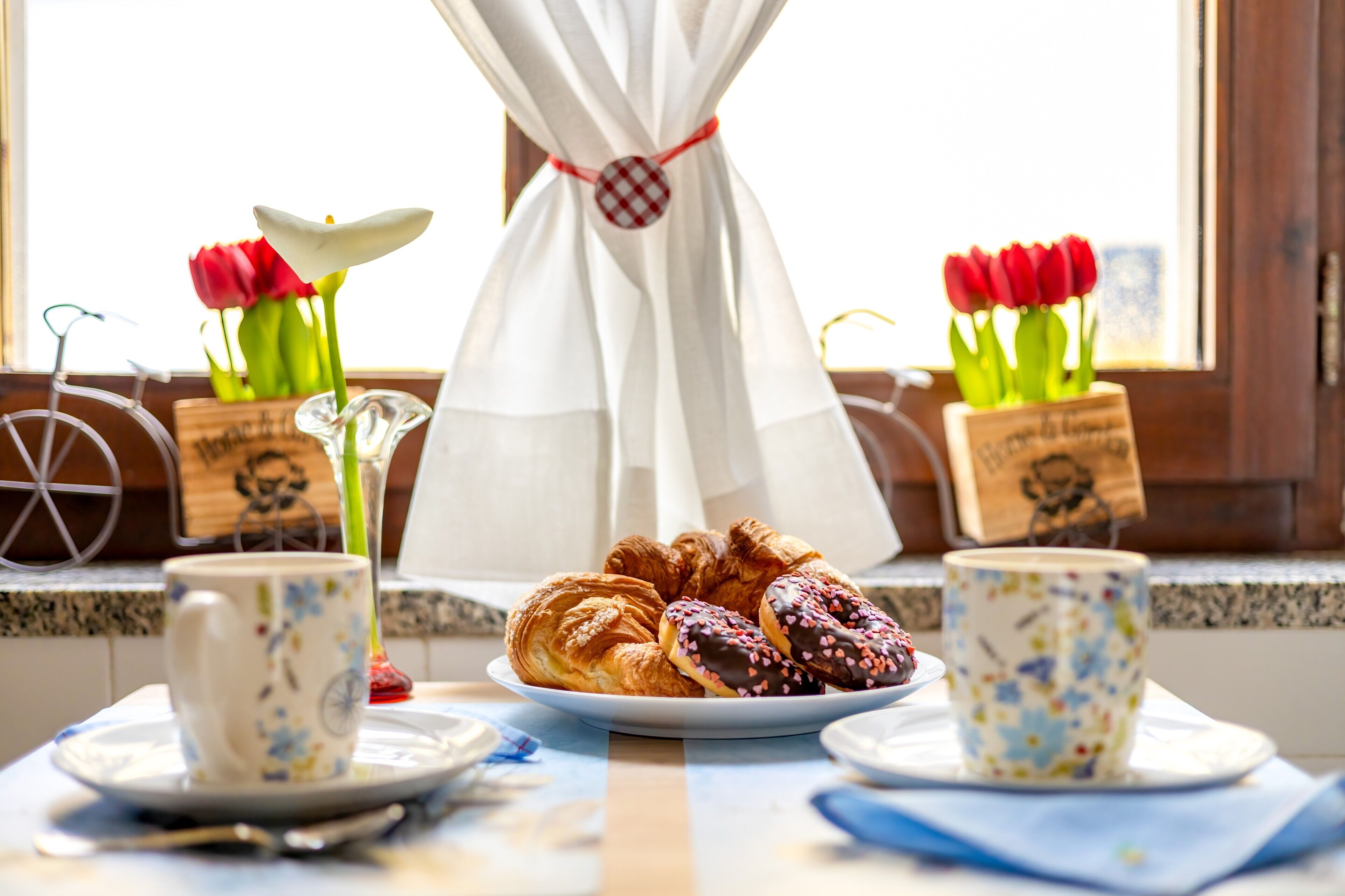 A breakfast setting with croissants, a cup, and tulips on a windowsill.