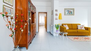 Ein Wohnzimmer mit einem Holzschrank, einem gelben Sofa, einem kleinen runden Tisch und einer Topfpflanze.
