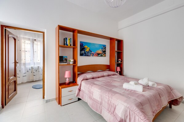 Un dormitorio con cama, un armario de madera, un cuadro y un baño visible a través de una puerta abierta.