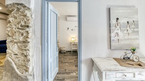 A hallway with a stone wall, a wooden floor, a white door, a small table with a bicycle, and a painting on the wall. - Apartment 'Ca La Maca' with Wi-Fi and Air Conditioning (Llançà)