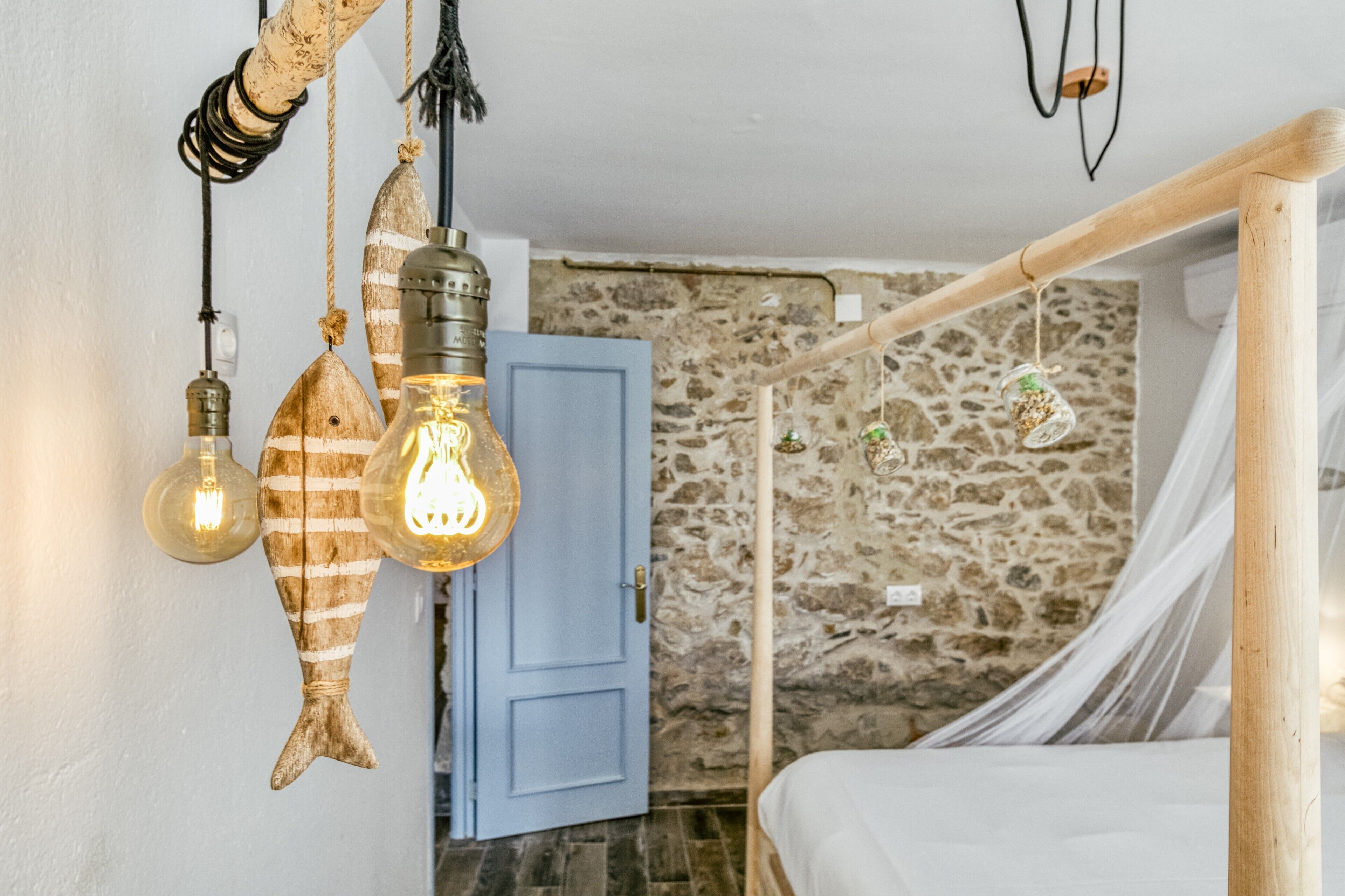 A bedroom with a stone wall, a wooden bed frame, and hanging light fixtures.