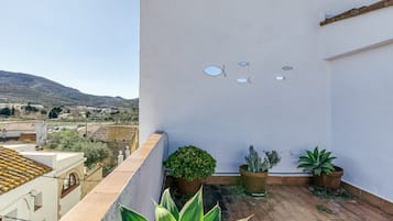 Terraza en la azotea con plantas en macetas, una pared blanca con adornos de peces y vistas a colinas distantes.