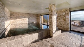 Ein Wellnessbereich mit Whirlpool, Steinwänden und Bergblick.
