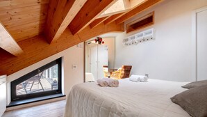 A bedroom with a sloped ceiling, a large bed with rolled towels, a wooden floor, and a window with a view. - Holiday Home "Relax e Felicità" Lake View, Private Jacuzzi, Shared Heated Indoor Pool (Perledo)