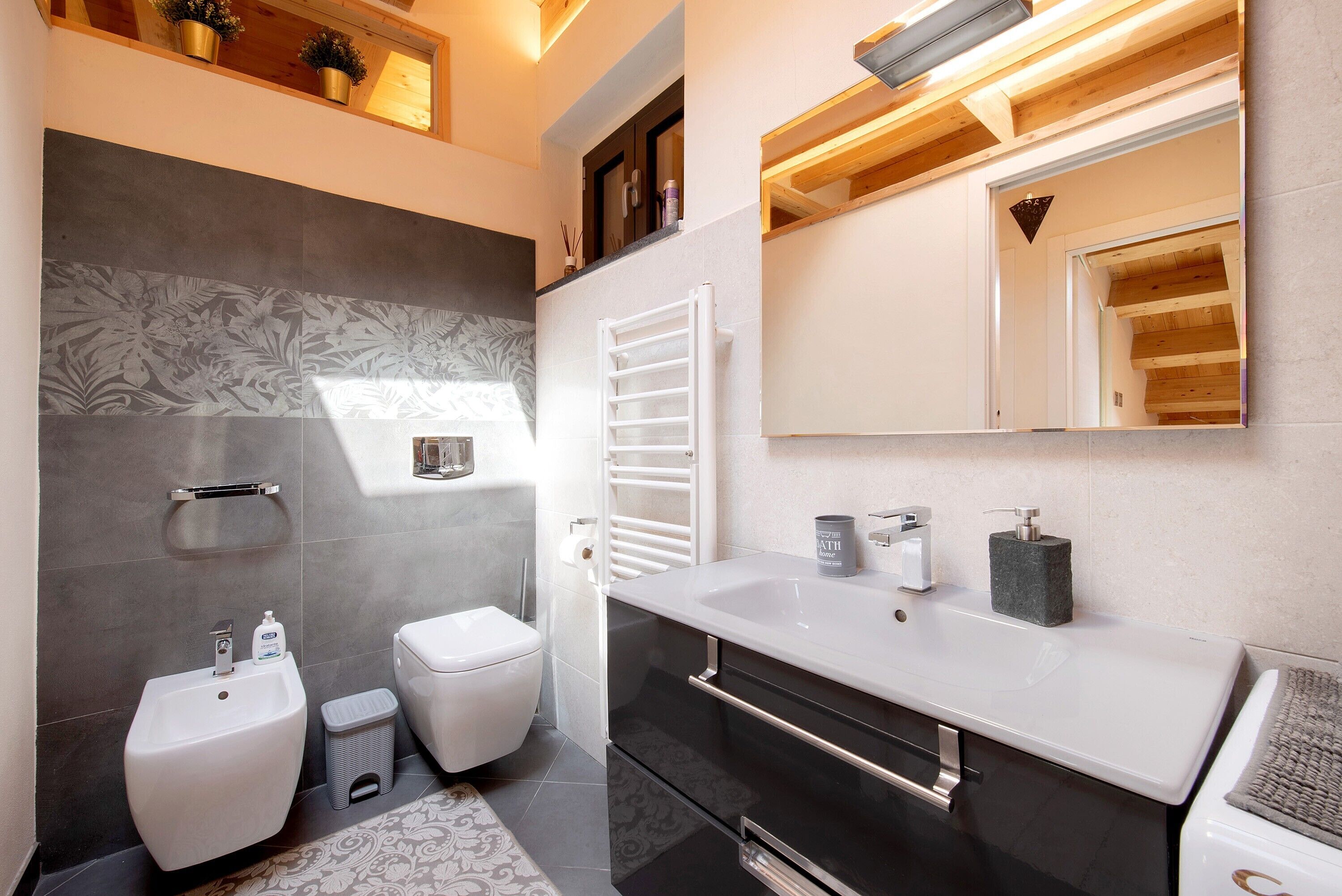 A modern bathroom with a bidet, toilet, vanity with a large mirror, and a towel rack.