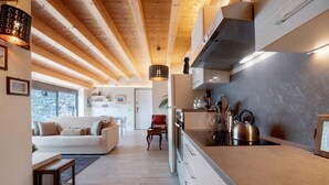 A modern kitchen with wooden beams, a dining area with a white sofa, and a view of a stone wall. - Holiday Home "Relax e Felicità" Lake View, Private Jacuzzi, Shared Heated Indoor Pool (Perledo)