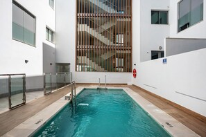 A swimming pool with glass railings, a wooden floor, and a staircase visible through the glass.