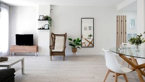 A modern living room with a TV, wicker chair, dining table, and potted plants. - Family Apartment 'Coral' with Private Pool, Wi-Fi and Air Conditioning (Conil de la Frontera)