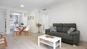 A modern living room with a grey sofa, white coffee table, and dining area with chairs and a glass table. - Family Apartment 'Coral' with Private Pool, Wi-Fi and Air Conditioning (Conil de la Frontera)