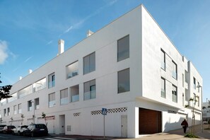 A modern building with multiple windows, a visible entrance, and a parking area.