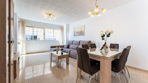 Un salon moderne avec une table à manger au plateau en verre, un canapé et un lustre.