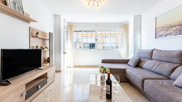 Un salon moderne avec un téléviseur à écran plat, un canapé, une table basse sur laquelle se trouvent une bouteille et des verres, et un tableau représentant un paysage urbain.