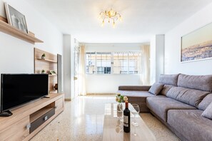 Un soggiorno moderno con una TV a schermo piatto, un divano, un tavolino da caffè con una bottiglia e dei bicchieri, e un dipinto con vista sulla città.