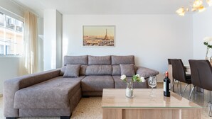 Un salon moderne avec un canapé d’angle, une table basse en verre et un coin repas avec des chaises.