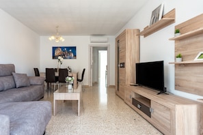 A modern living room with a sofa, TV, wooden entertainment unit, dining table, chairs, and a painting of a building. - Apartment 'Fuengirola' with Balcony, Wi-Fi and Air Conditioning (Fuengirola)