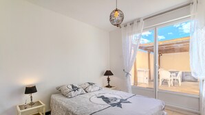 Et soveværelse med seng, et sengebord med lampe, et vindue med gardiner og udsigt til en udendørs patio.