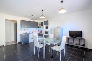 Una cocina moderna con comedor, sillas blancas, una mesa de vidrio y un televisor sobre un mueble.