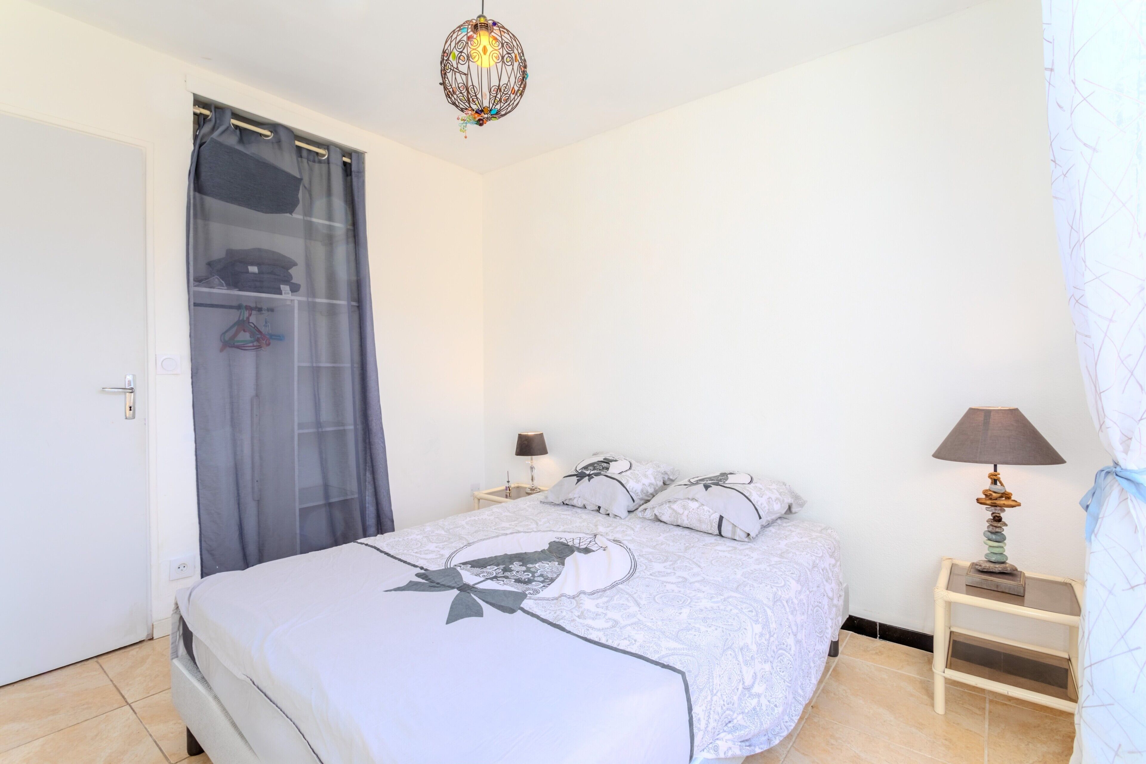 Une chambre à coucher avec un lit, une table de chevet avec une lampe, un luminaire suspendu et une porte avec un rideau.