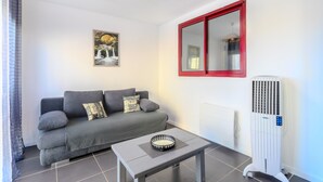 En stue med en grå sofa, et lille bord, en hvid radiator og en gulvvarmer.