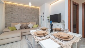 A modern living room with a stone wall, a sofa, a dining table set with plates and glasses, and a television on a stand.