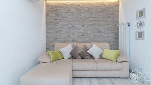 A modern living room with a stone accent wall, a sectional sofa with cushions, a white radiator, and decorative wall art.
