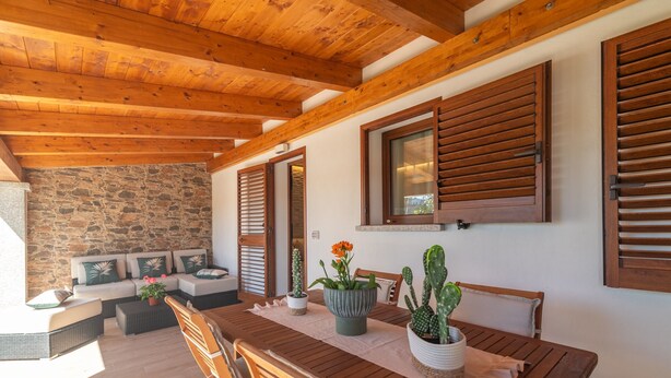 A wooden dining table with chairs, a stone wall, and wooden shutters.