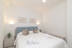 A neatly made bed with rolled towels, a blue headboard, and two wall-mounted light fixtures.