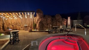 A hot tub with a red light, surrounded by outdoor seating and a rock wall backdrop. - Sage Creek Condo E2 - "Amazing Pool & Hot Tubs" (Moab)
