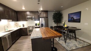 A modern kitchen with dark wood cabinets, stainless steel appliances, a central island, and a dining area with a table and chairs. - Sage Creek Condo E2 - "Amazing Pool & Hot Tubs" (Moab)