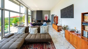 Uma sala de estar moderna com um amplo sofá modular, uma estante de madeira e uma grande janela com vista para o exterior.