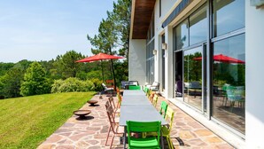 Um pátio externo com uma mesa comprida, cadeiras e guarda-sóis vermelhos.