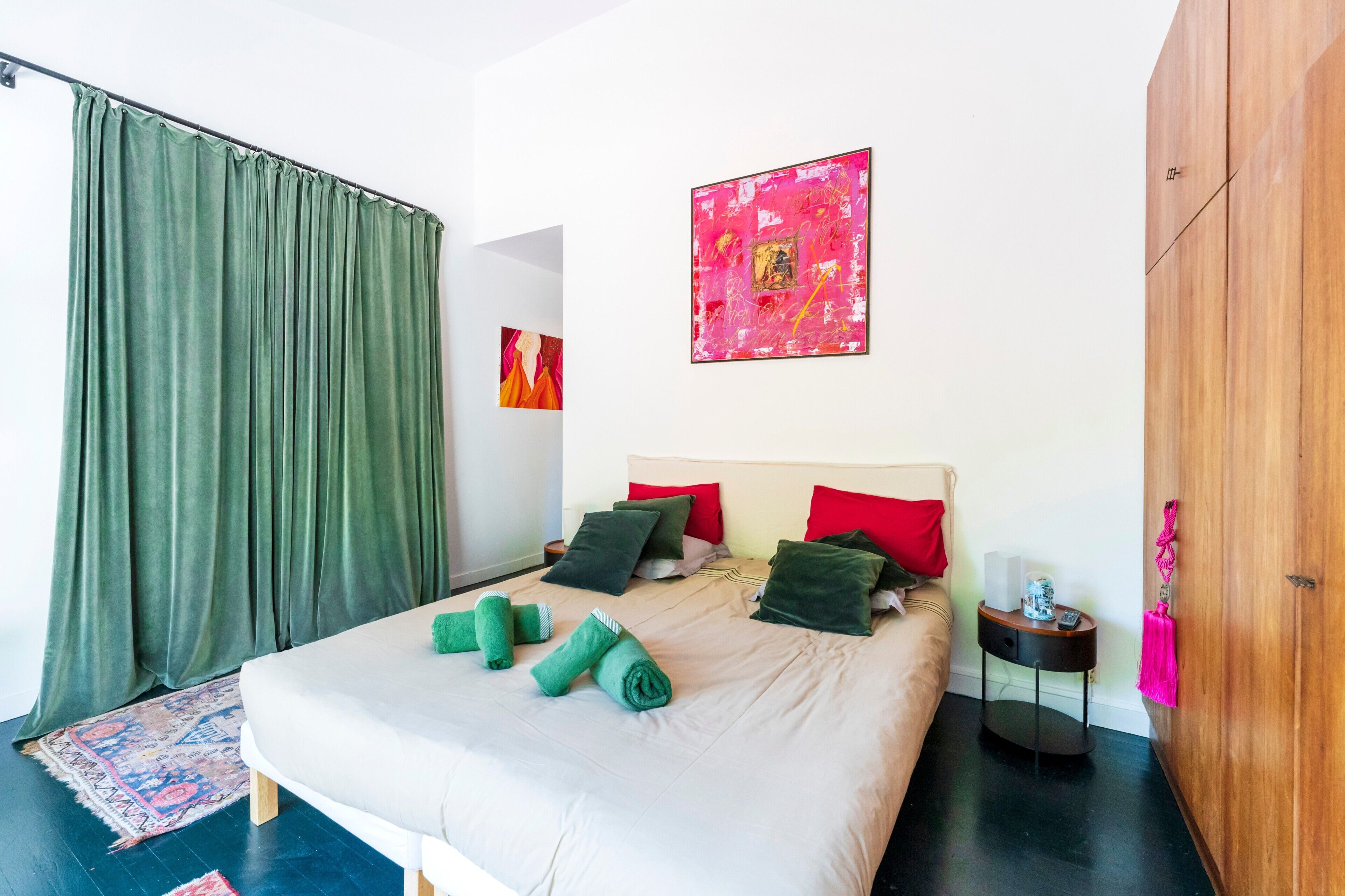 Habitación de hotel con cama, cortinas verdes, un cuadro abstracto rojo y un armario de madera.