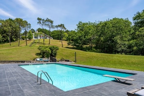 Une piscine rectangulaire avec une terrasse carrelée, une échelle en métal et une table de pique-nique en bois.