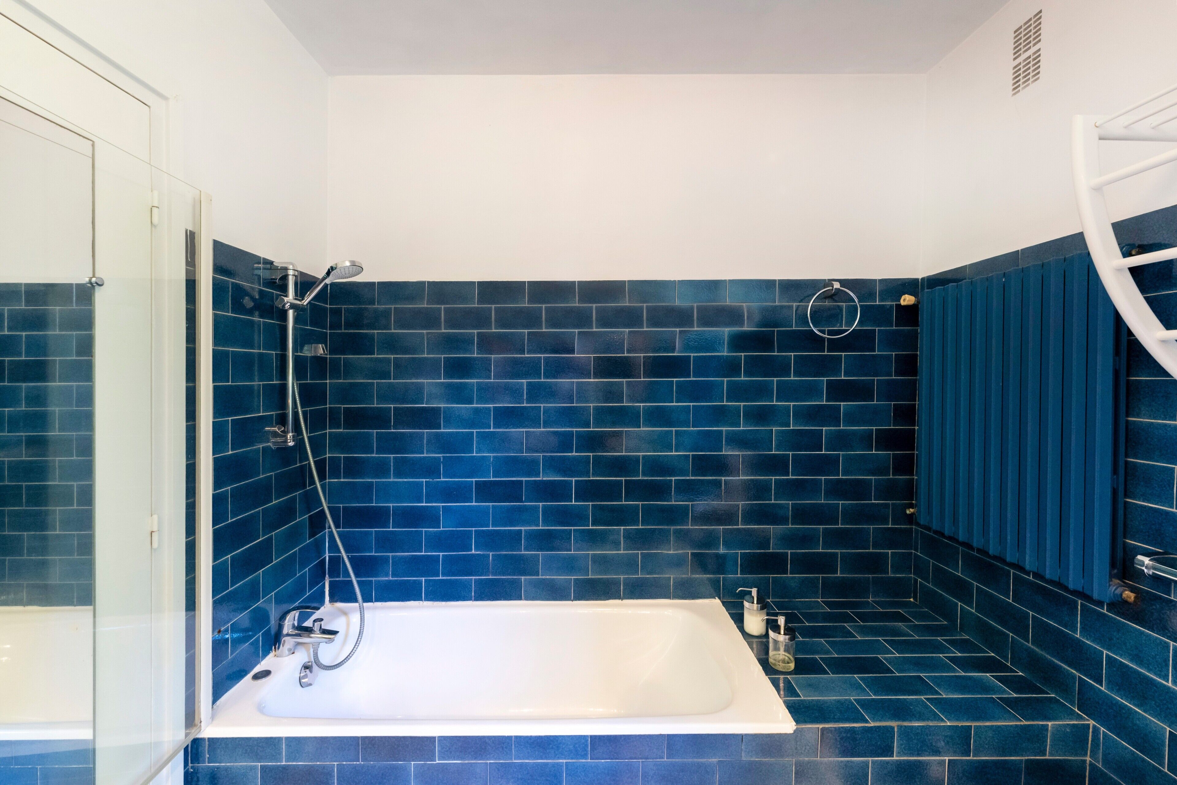 A bathroom with a white bathtub, a glass shower enclosure, and blue-tiled walls.