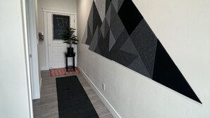 En gang med geometrisk vægkunst, en sort måtte og en dør med et velkommenskilt.