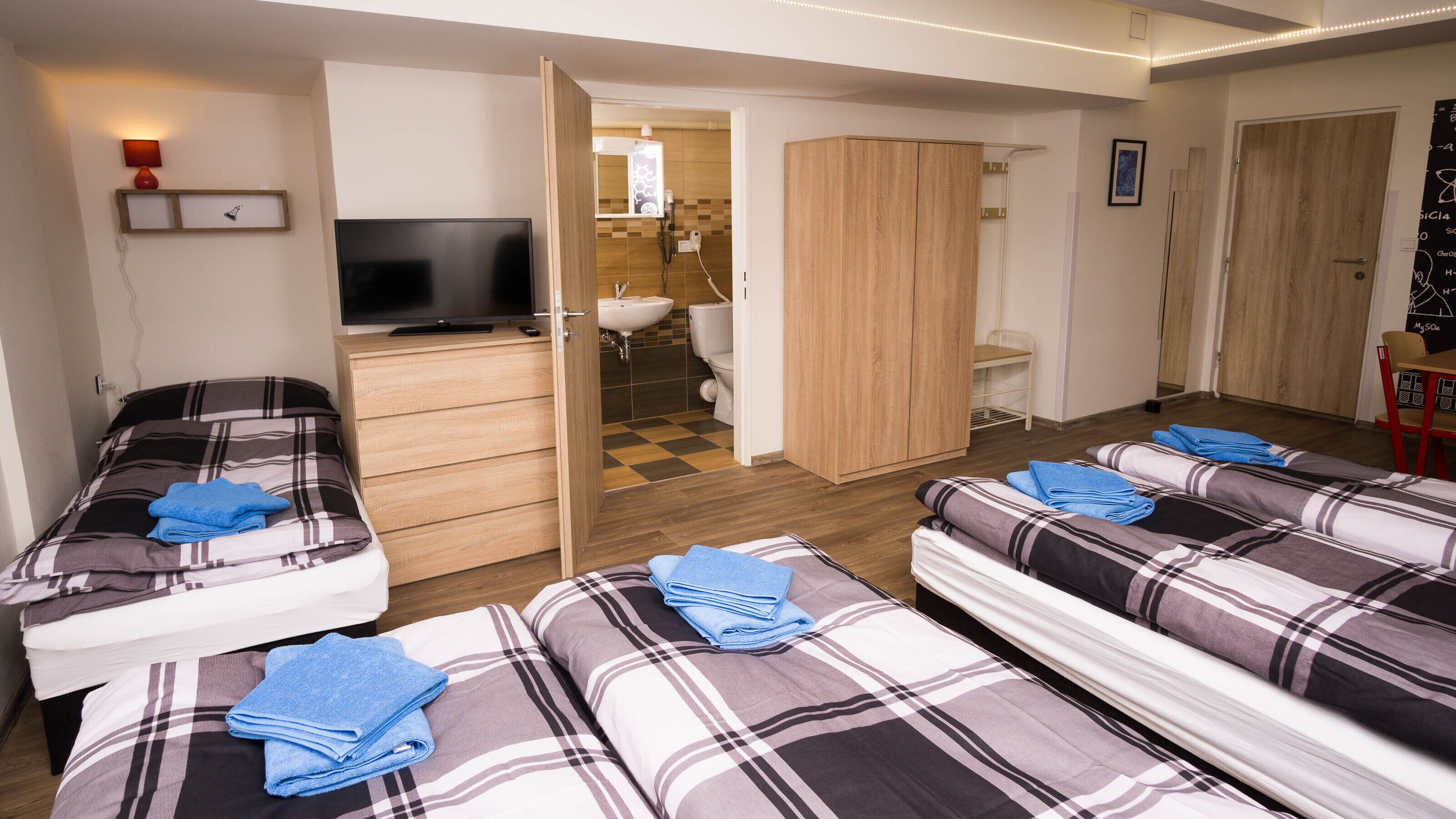 A hotel room with two beds, a TV, a wardrobe, and a bathroom visible through an open door.