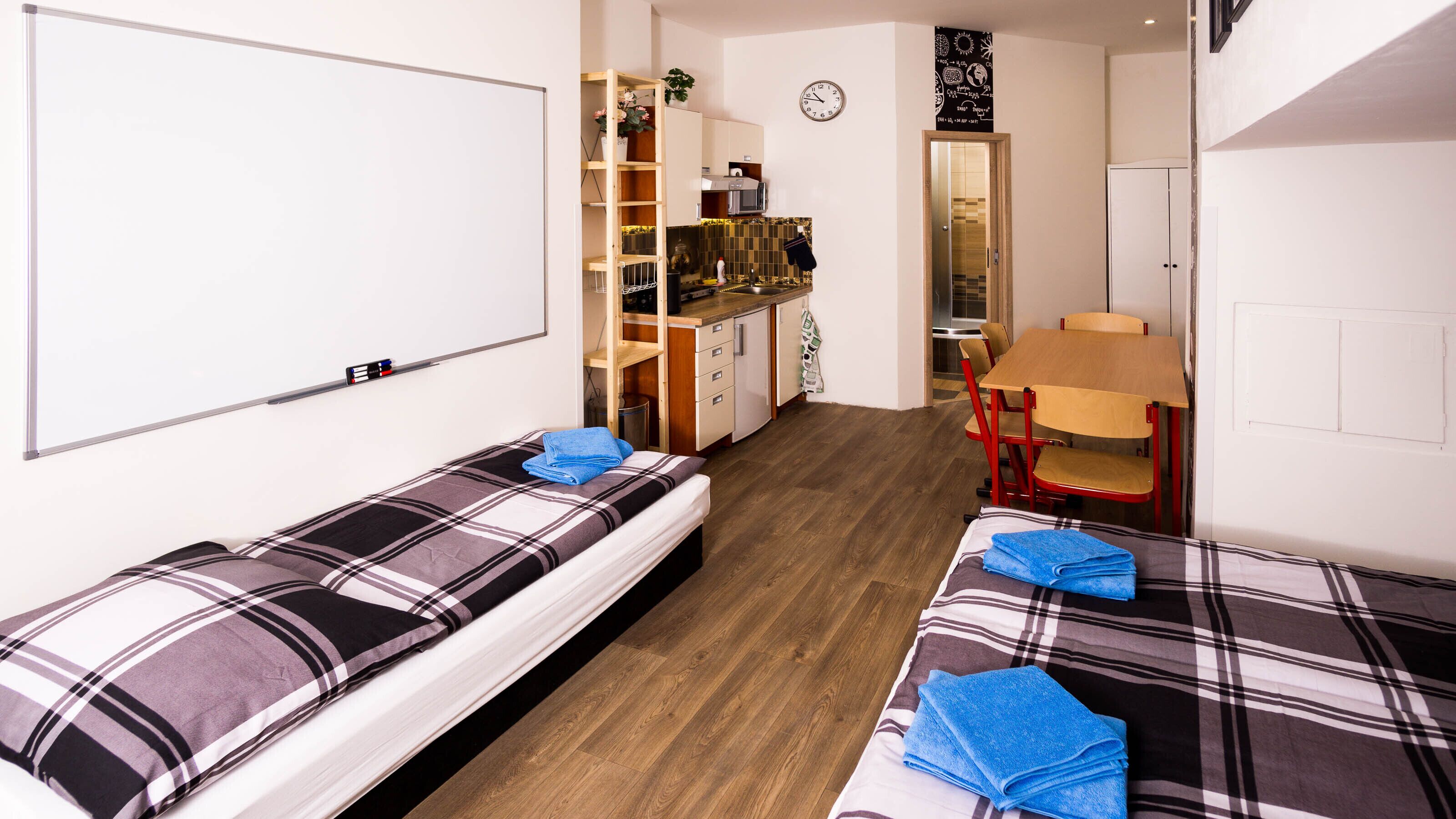 Una habitación compacta con dos camas, un pequeño kitchenette, una mesa de comedor y un reloj en la pared.