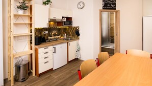 Een kleine keuken met een magnetron, fornuis en spoelbak. Er is een eettafel met stoelen en een afvalbak.