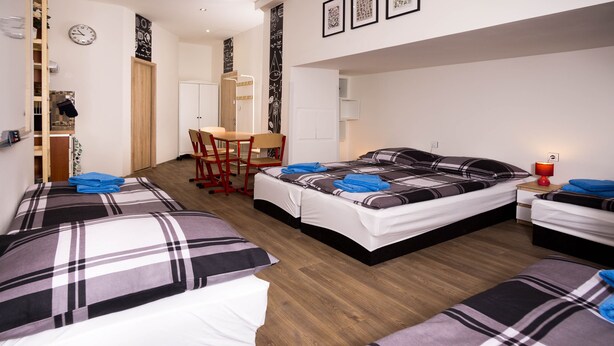 Een hotelkamer met een bed, een bureau en een stoel. Er hangt een klok aan de muur en er is een raam.