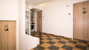 Een gang met een zwart-wit geruit vloerkleed, een wasmachine en een glazen deur naar een kamer.