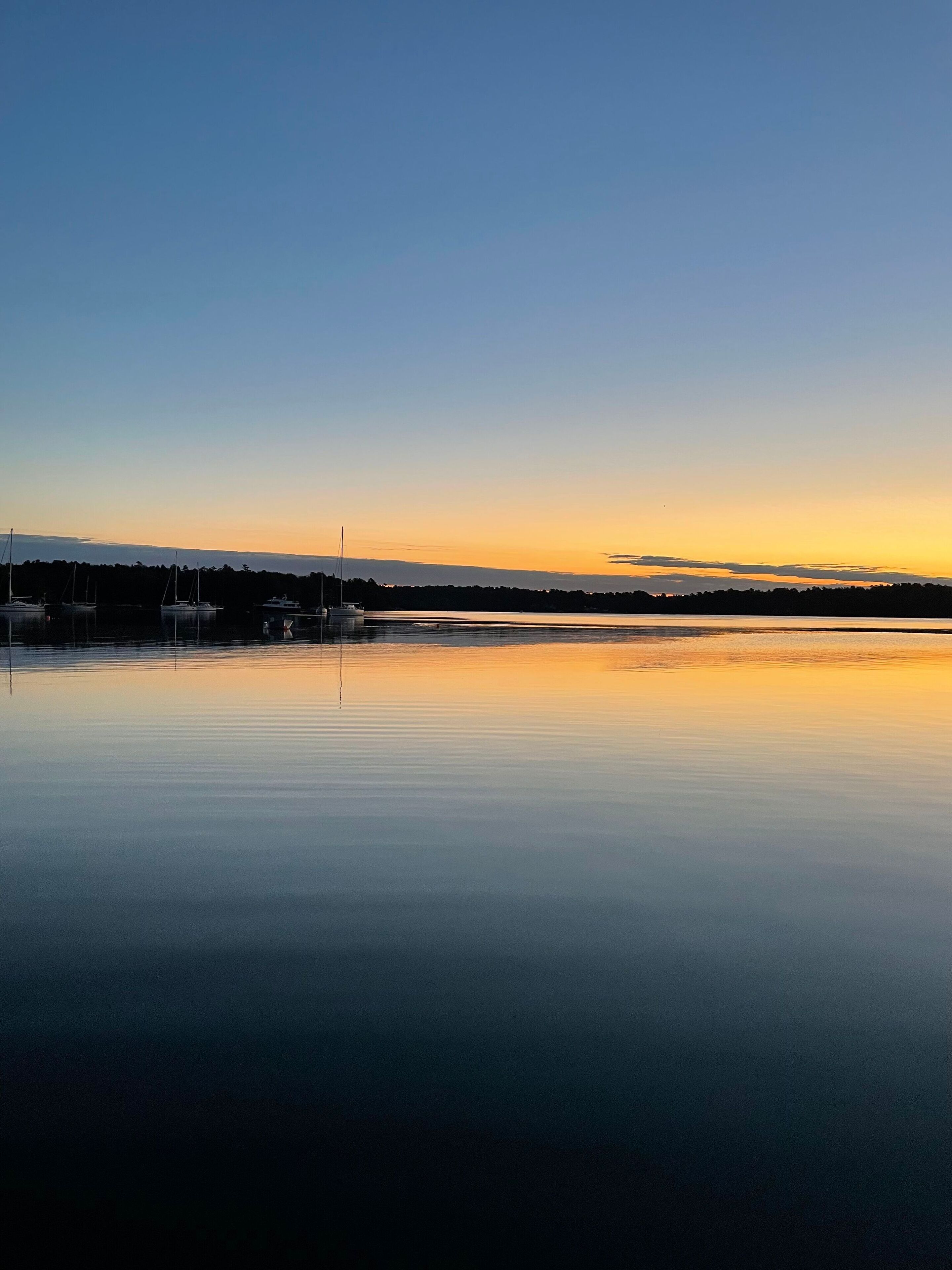 Ein ruhiger See bei Sonnenuntergang mit Booten und einer entfernten Küstenlinie.