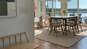 A spacious room with a large dining table, wooden chairs, a bench, and a view of the outdoors through large windows. - Coveshead. Dramatic waterfront designer cottage. (Harpswell)